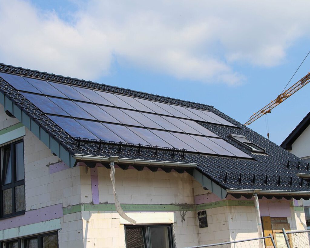 Installation von Solarpanelen auf einem Rohbau, mit Kran vor blauem Himmel im Hintergrund